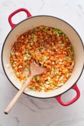 Diced celery, carrots, and onions cooking in a white enamel pot with red handles, preparing healthy ingredients for nutritious recipes at Food Faith Fitness.