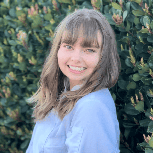 Bright young woman smiling outdoors with lush green foliage, showcasing healthy lifestyle, wellness, and positivity.