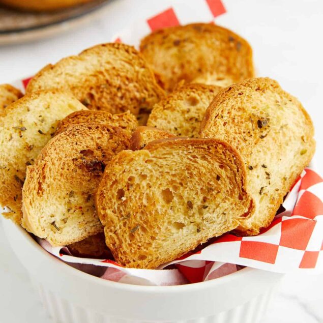 Golden brown garlic bread slices in a white ramekin with red checkered paper, showcasing healthy bread options and delicious recipes from Food Faith Fitness.