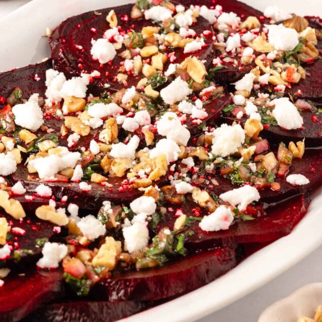 Sweet roasted beets topped with crumbled feta cheese, chopped walnuts, and fresh herbs, served in a white oval dish. A healthy, colorful, and nutrient-rich vegetable dish perfect for maintaining a balanced diet.