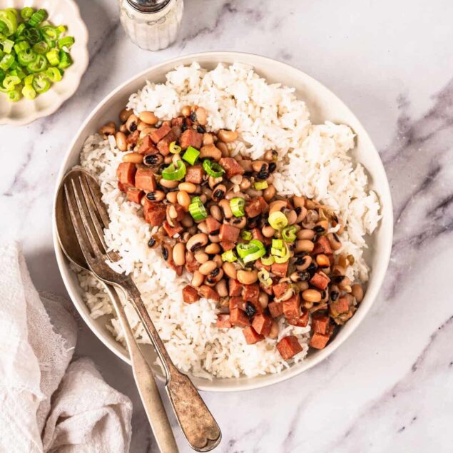 Savory black-eyed pea and rice bowl garnished with green onions on a white marble background, healthy vegan meal, food faith fitness, high-protein plant-based dish, easy nutritious recipe for weight loss.