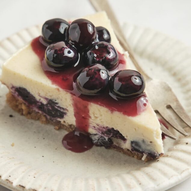 Fresh blueberry cheesecake with creamy filling, graham cracker crust, and blueberry topping on a white plate. Perfect for healthy dessert recipes and indulging guilt-free.