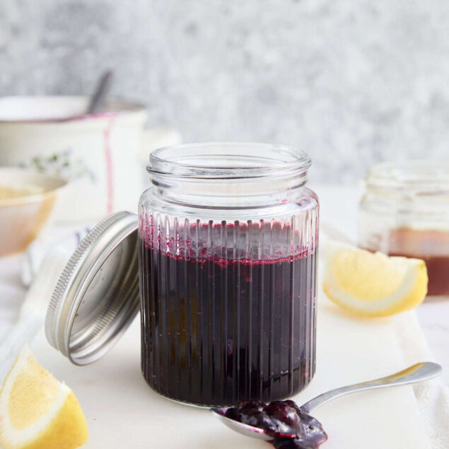 Fresh homemade blueberry lemon syrup in a glass jar with lemon wedges, perfect for healthy recipes and food cravings.