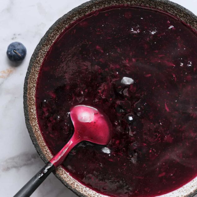 Homemade blueberry jam in a rustic bowl with a spoon on a white marble surface for healthy eating and nutritious recipes.