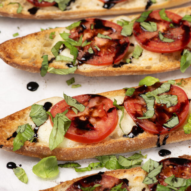 Fresh baked garlic bread topped with ripe tomatoes, fresh basil, and balsamic glaze, perfect for a healthy and delicious meal option at Food Faith Fitness.
