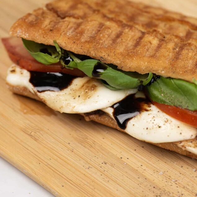 Grilled fish sandwich with fresh vegetables, mozzarella, and balsamic glaze on a wooden serving board. Perfect for healthy eating and balanced meals from Food Faith Fitness.