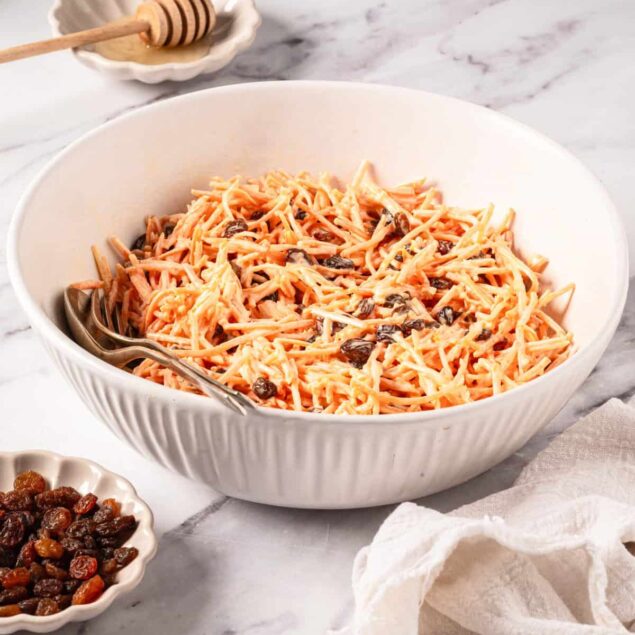 Creamy vegan spaghetti with sun-dried tomatoes in a white bowl, served with a small dish of honey and a drizzle of olive oil, featuring a light and healthy meal option.