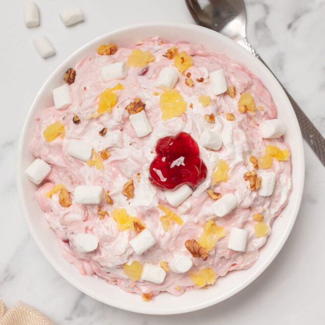 Sweet cherry yogurt with marshmallows and lemon zest on a white bowl.