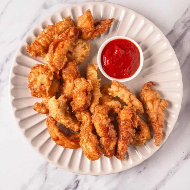 Crispy fried chicken tenders with a side of classic red dipping sauce on a white ceramic plate. Perfect for healthy eating and meal prep, highlighting nutritious food choices and delicious chicken recipes.