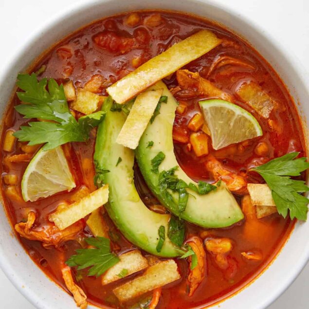 Savory vegetable and chicken tortilla soup with fresh avocado, lime, and cilantro in a white bowl, healthy recipe ideas for weight loss and nutritious meals.