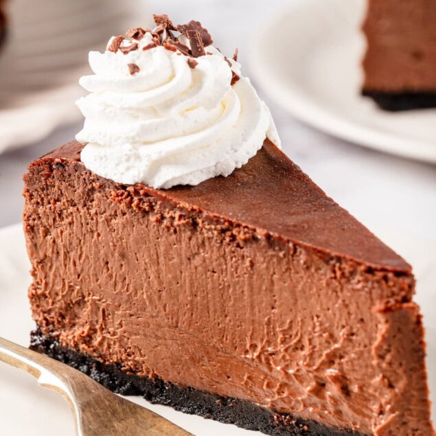 Rich chocolate cheesecake with whipped cream topping and chocolate shavings, served on a white plate with a fork, perfect for dessert lovers on food faith fitness.