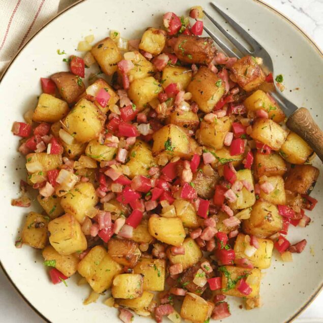 Crispy roasted potatoes with bacon and herbs on a white plate.