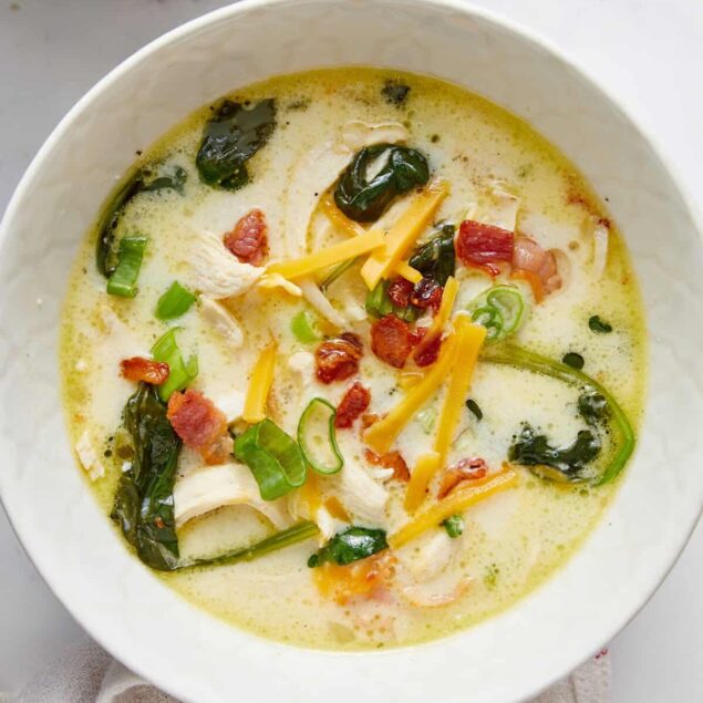 Creamy chicken and vegetable soup with bacon, shredded cheese, and green onions in a white bowl, healthy comfort food option, perfect for meal prep or cozy dinners, gluten-free recipe, nutritious and delicious.