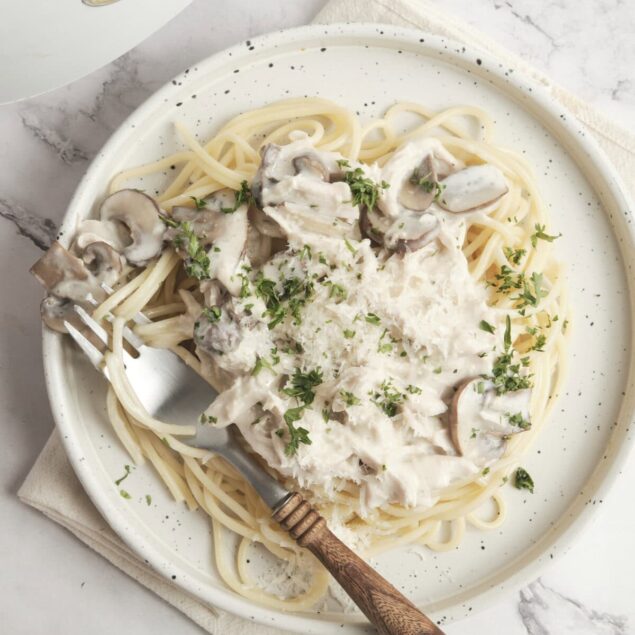 Creamy mushroom chicken alfredo pasta served on a white speckled plate with fresh parsley garnish. A light, healthy, and delicious meal perfect for food lovers and fitness enthusiasts.