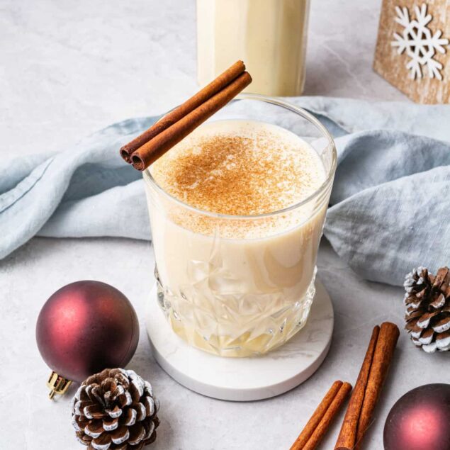 Creamy eggnog recipe with cinnamon sticks, pinecones, and holiday decorations for festive season. Perfect for Christmas desserts and holiday celebrations.