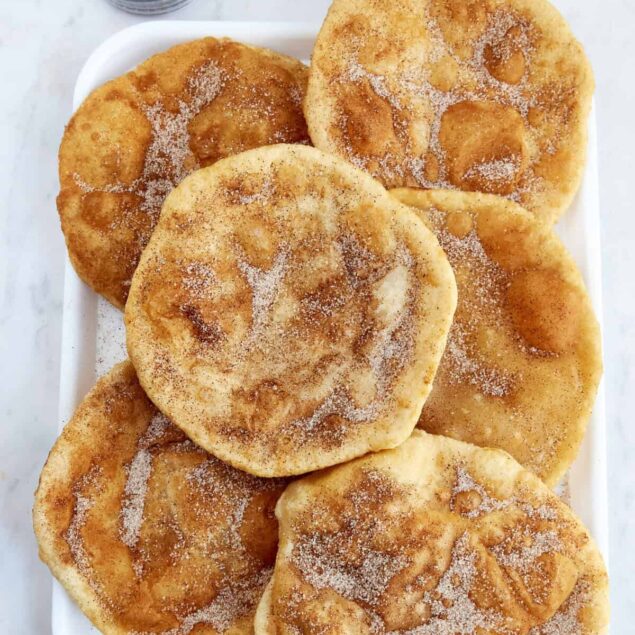 Golden fried plantains dusted with cinnamon sugar on a white platter, healthy snack, tasty and nutritious, plant-based dessert, food faith fitness, tropical fruit recipe, gluten-free snack.