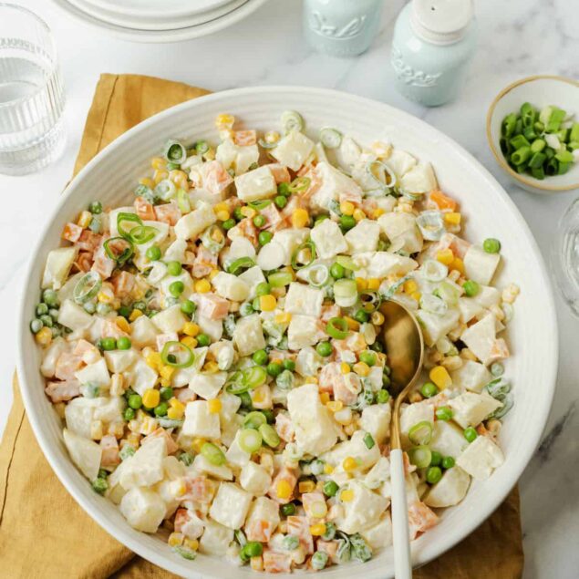 Creamy chicken salad with peas, carrots, and scallions in a large white bowl, healthy meal prep option, on a white marble surface with salt and pepper shakers.