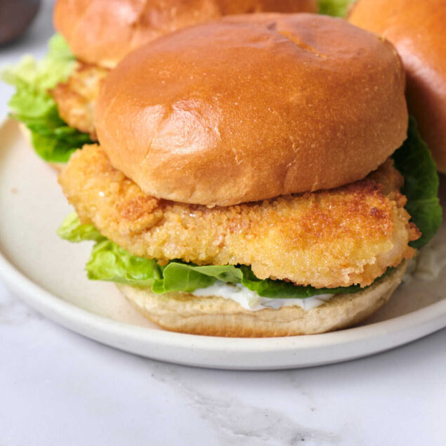 Crispy fried chicken sandwich with lettuce and creamy sauce on a toasted bun, served on a white plate. Perfect for healthy fast food options and meal prep ideas from Food Faith Fitness.