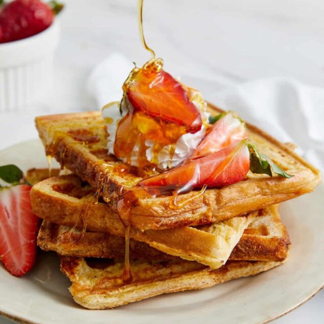 Sweet waffle topped with fresh strawberries, whipped cream, and drizzled honey, showcasing a healthy breakfast recipe from Food Faith Fitness.