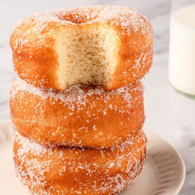 Fluffy glazed donuts stacked on a white plate, perfect for breakfast or a snack, showcasing indulgent comfort food with a sweet sugar coating.
