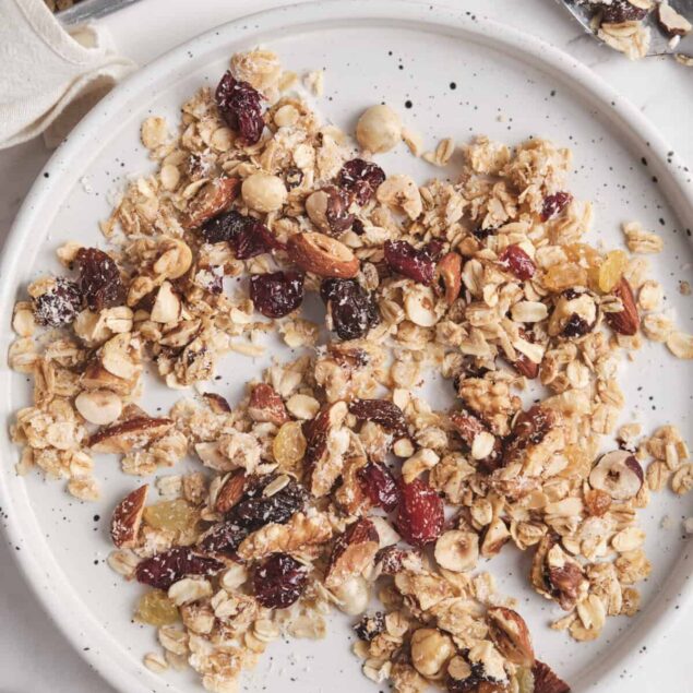 Crunchy homemade healthy granola with nuts, seeds, and dried fruit on a white plate, ideal for wholesome snacking and breakfast. Perfect for a nutritious lifestyle aligned with Food Faith Fitness principles.