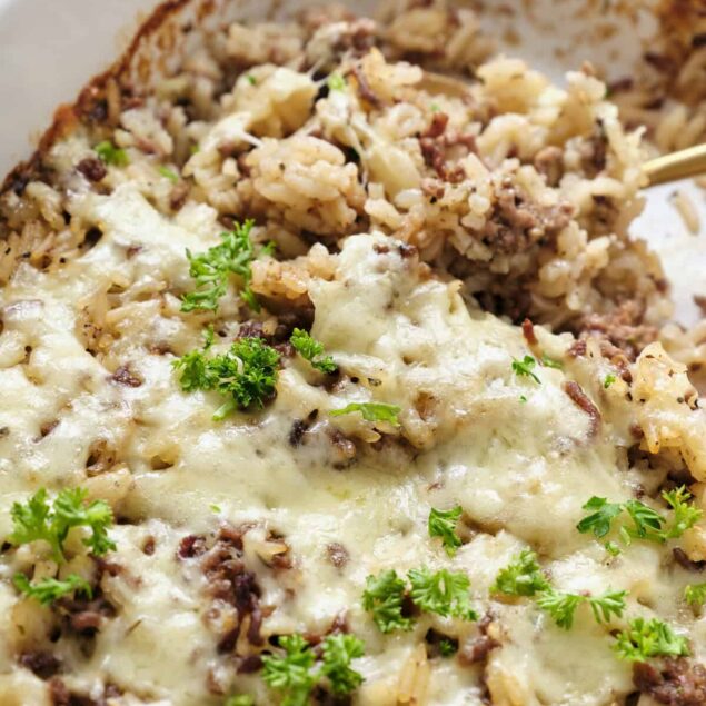 Savory baked casserole with melted cheese, ground beef, rice, and herbs in a white dish for healthy comfort food recipes.