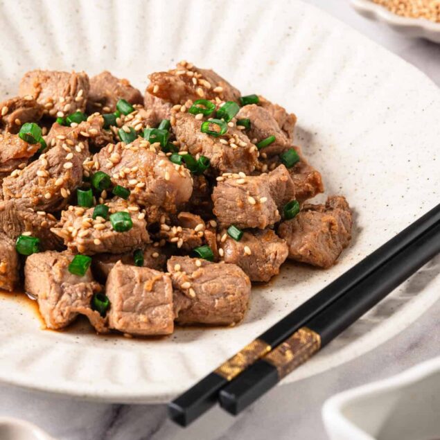 Tender beef cubes stir-fried with sesame seeds and chopped green onions, served on a minimalist white dish, perfect for healthy meals and homemade Asian-inspired recipes.