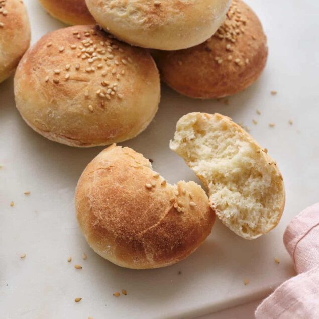 Soft, homemade dinner rolls with a golden crust and sprinkled sesame seeds on top, arranged on a white cutting board, perfect for healthy eating and meal prep.
