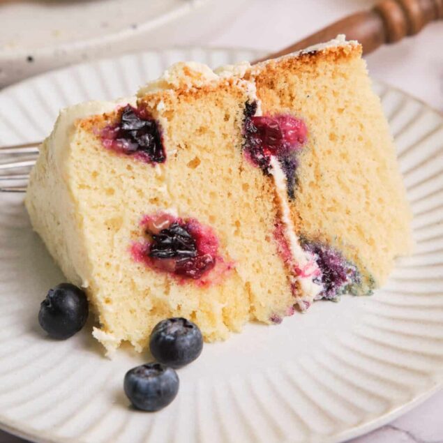 Blueberry lemon cake with fresh berries on a white plate, perfect for healthy dessert recipes. Delicious, moist, and flavorful, this cake combines fresh blueberries and zesty lemon for a wholesome treat.