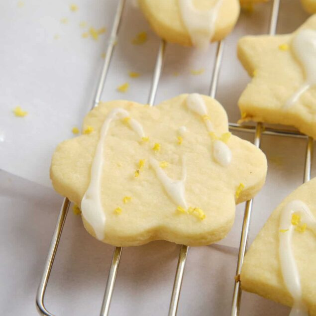 Buttery lemon sugar cookies with white chocolate drizzle and lemon zest on a cooling rack, perfect for healthy dessert recipes and lemon-flavored treats.