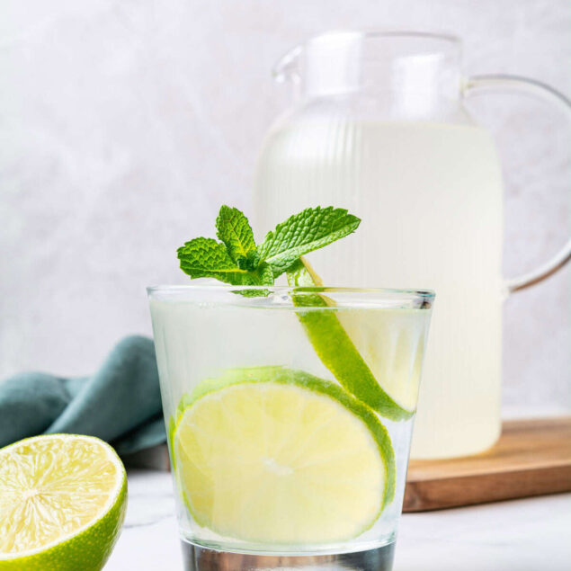 Fresh lemon and mint infused water in a glass with a pitcher in the background, promoting healthy hydration and clean eating. Perfect for weight loss and wellness, featured on Food Faith Fitness.
