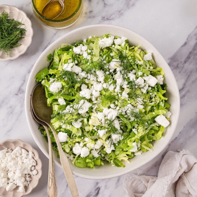 Fresh green salad with feta cheese, dill, and a vinaigrette dressing on marble surface. Healthy, nutritious meal for weight loss and wellness. Perfect for a clean eating lifestyle.