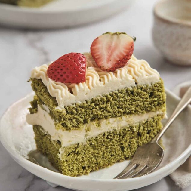 Rich green matcha cake with creamy frosting and fresh strawberries on top, served on a white plate, highlighting healthy dessert options and delicious recipes from Food Faith Fitness.