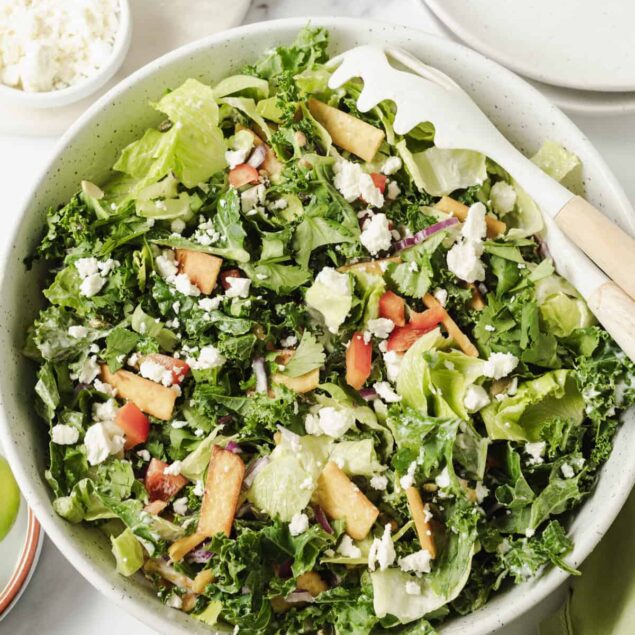 Fresh vegetable salad with lettuce, kale, red peppers, feta cheese, and croutons in a white bowl, healthy meal option on Food Faith Fitness recipe blog.