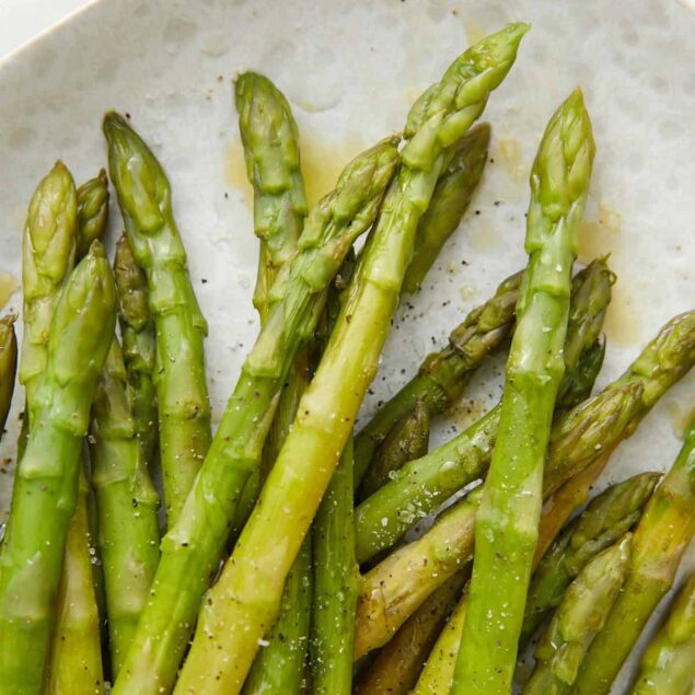 Fresh roasted asparagus spears drizzled with olive oil, seasoned with salt and pepper, on a white plate. A nutritious, healthy vegetable side dish perfect for balanced eating and fitness-focused meals.