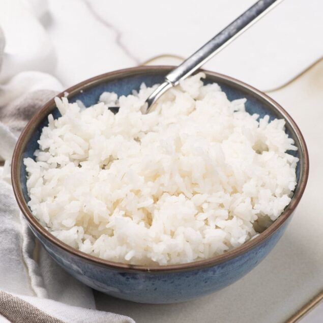 Fluffy cooked white rice in a blue ceramic bowl, healthy meal prep idea, high-carb vegetarian side dish for balanced diet.