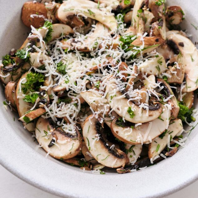 Fresh mushroom salad topped with shredded cheese and fresh herbs, healthy and delicious vegan-friendly meal option.