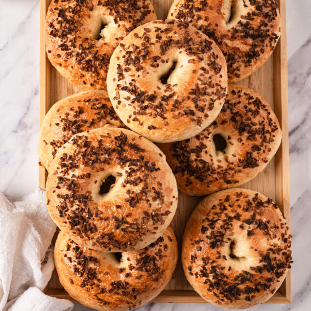 Golden brown bagels topped with chocolate chips on a wooden tray in a breakfast setting.