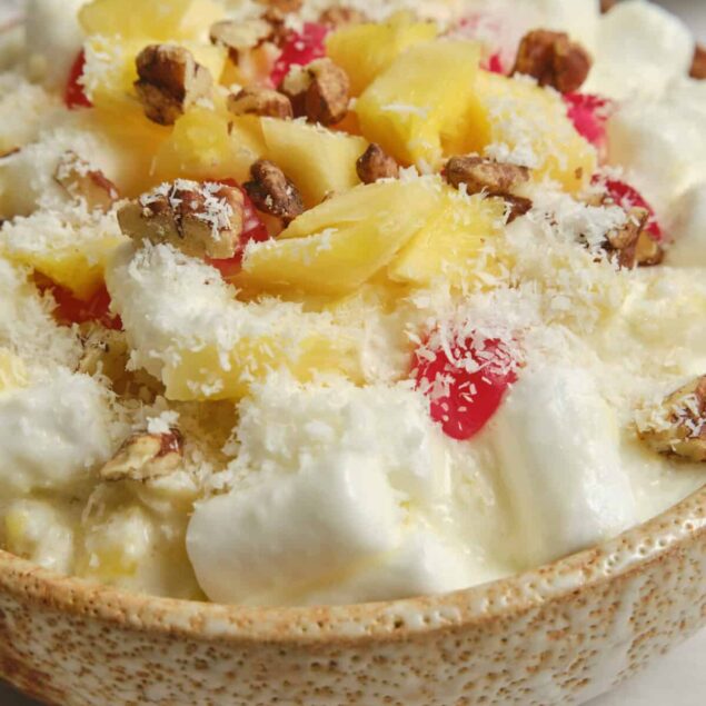 Creamy fruit salad with pineapple, coconut flakes, and chopped pecans in a textured bowl, showcasing a healthy, delicious dessert option from Food Faith Fitness.
