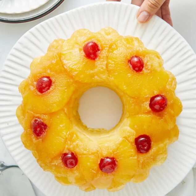 Sweet pineapple upside-down cake with cherries on a white plate, vibrant and appealing dessert, perfect for healthy eating and fitness-focused recipes.