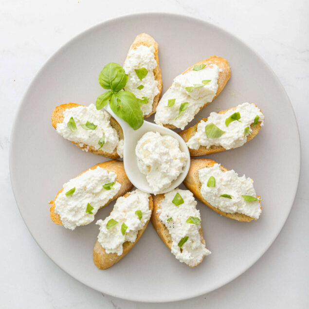 Cream cheese basil crostini appetizer, served on a white plate with fresh basil garnish, perfect for healthy snacks or party appetizers.