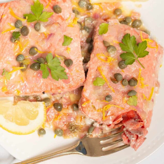 Succulent baked salmon with lemon, capers, and fresh herbs on a white plate, ideal for healthy eating and nutritious meals. Perfect for clean eating and weight loss diets.