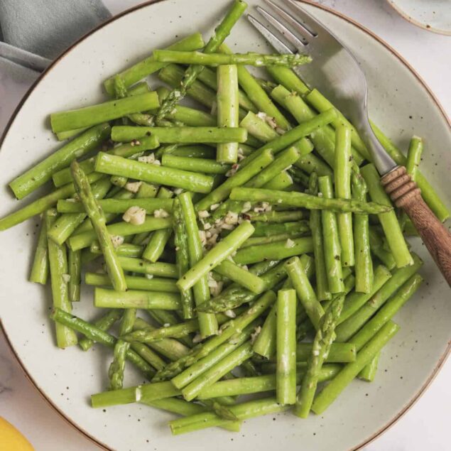 Steamed fresh asparagus spears garnished with garlic in a white bowl, healthy and nutritious vegetable side dish for a balanced diet.
