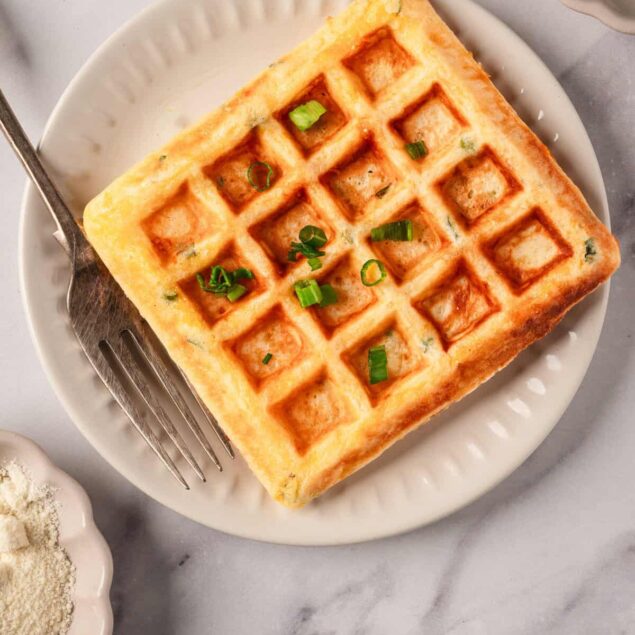Crispy golden waffle topped with chopped green onions on a white plate, served as a healthy breakfast or snack option from Food Faith Fitness.