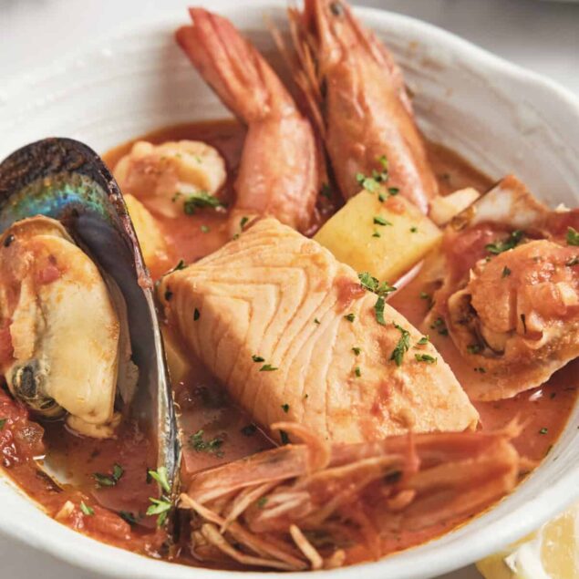 Succulent seafood stew with salmon, shrimp, and mussels in savory tomato broth, garnished with fresh herbs and lemon wedge, healthy fish dish from Food Faith Fitness.