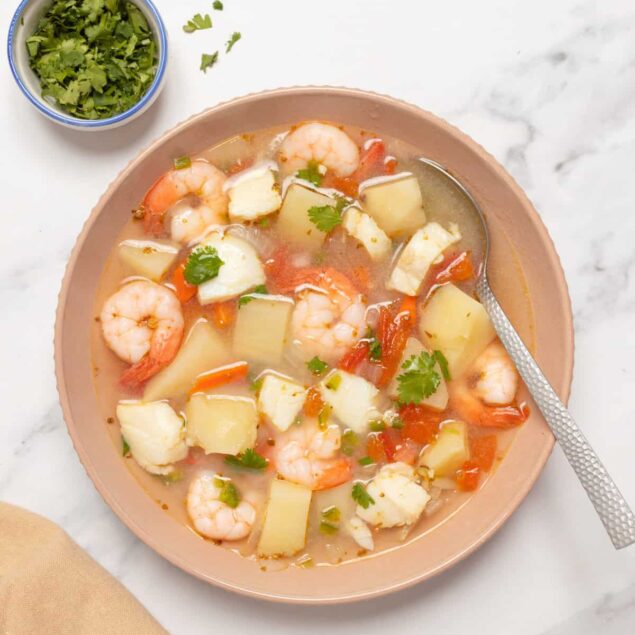 Creamy shrimp and vegetable soup with potatoes, carrots, and fresh cilantro on a white marble surface. Perfect for healthy, nourishing meals.