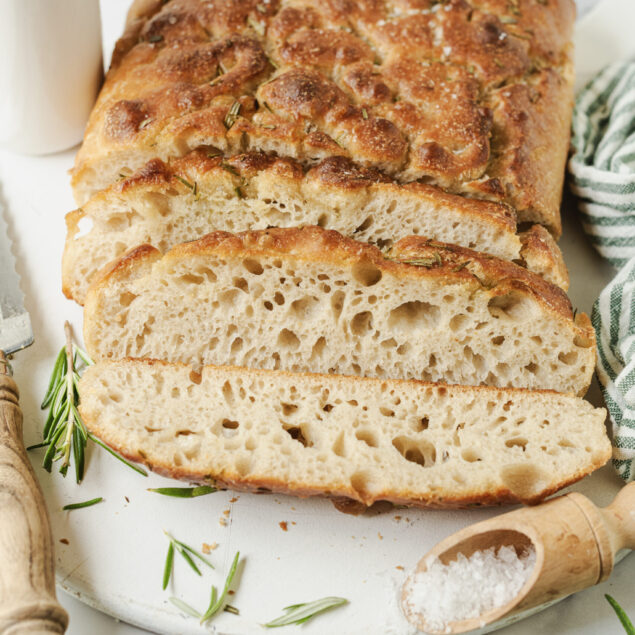 Soft and airy homemade focaccia bread with herbs on a white cutting board. Perfect for healthy eating, meal prep, and gluten-free recipes. Fresh and delicious bakery-style bread.