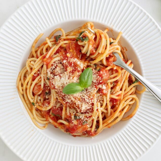 Creamy spaghetti with tomato sauce, fresh basil, and grated cheese served on a white plate, highlighting healthy and delicious meal ideas from Food Faith Fitness.