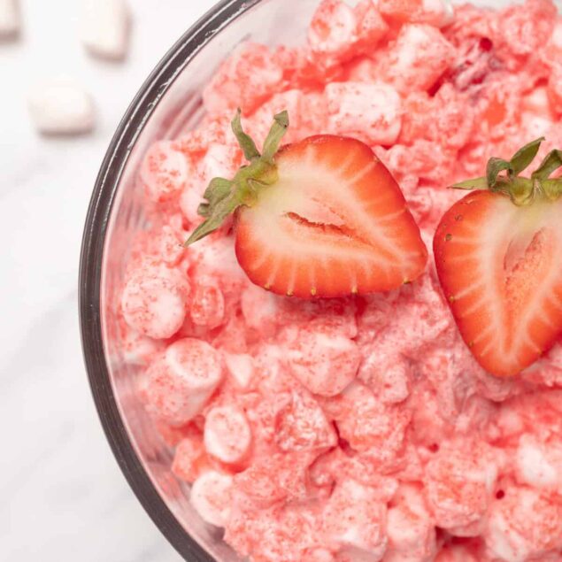 Fresh strawberry flavored whipped cottage cheese with raspberries topped with two halved strawberries on a white marble surface.