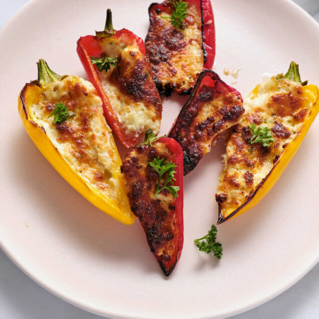 Roasted stuffed bell peppers with melted cheese and fresh herbs on a white plate, healthy meal, gluten-free, low-carb, high-protein, vegan options, Food Faith Fitness recipes.
